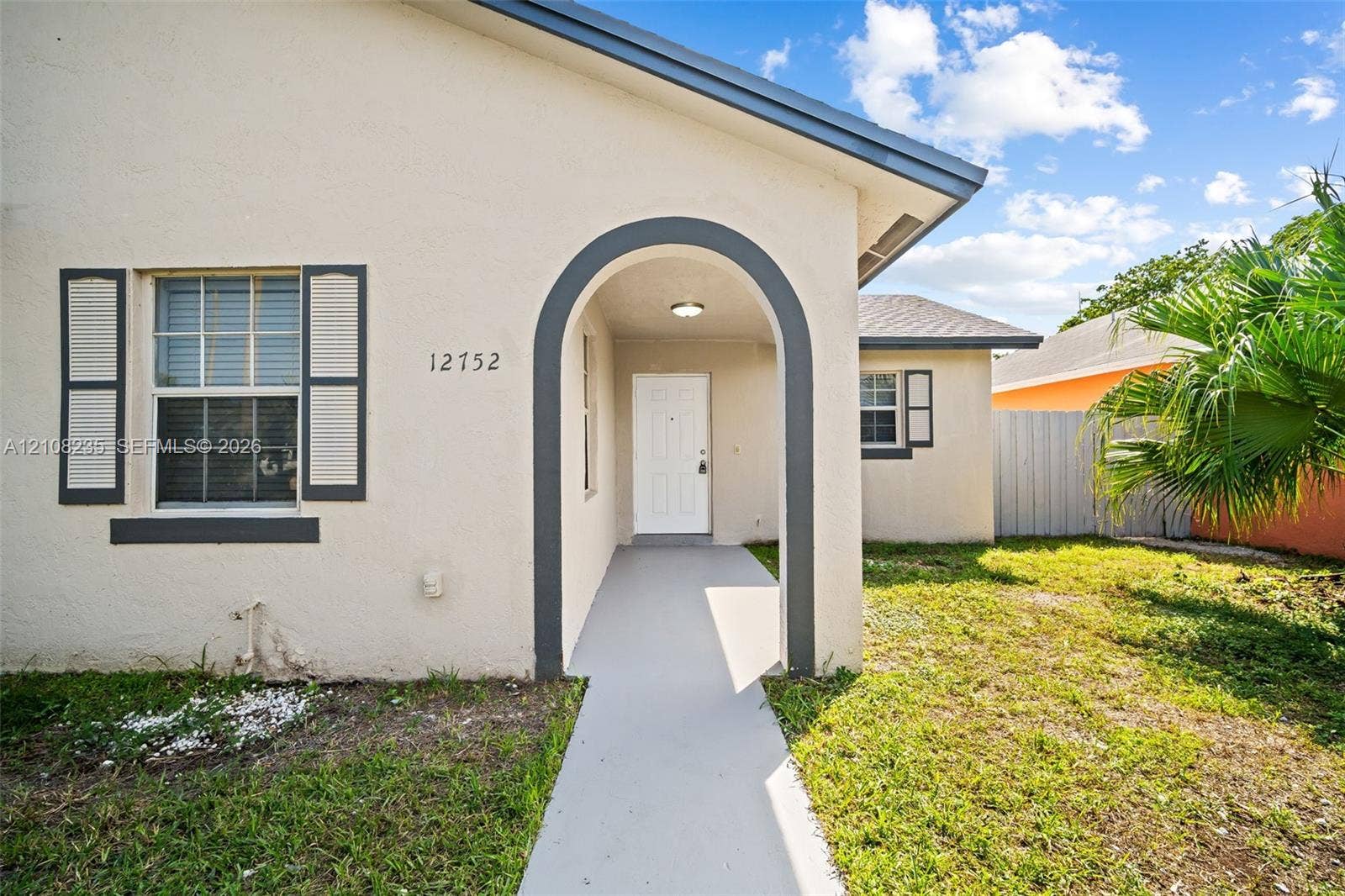 12752 SW 250th Terrace, Homestead, FL 33032 Stucco exterior featuring a covered arched entryway, grey-trimmed window shutters, a concrete walkway, and a hip roof