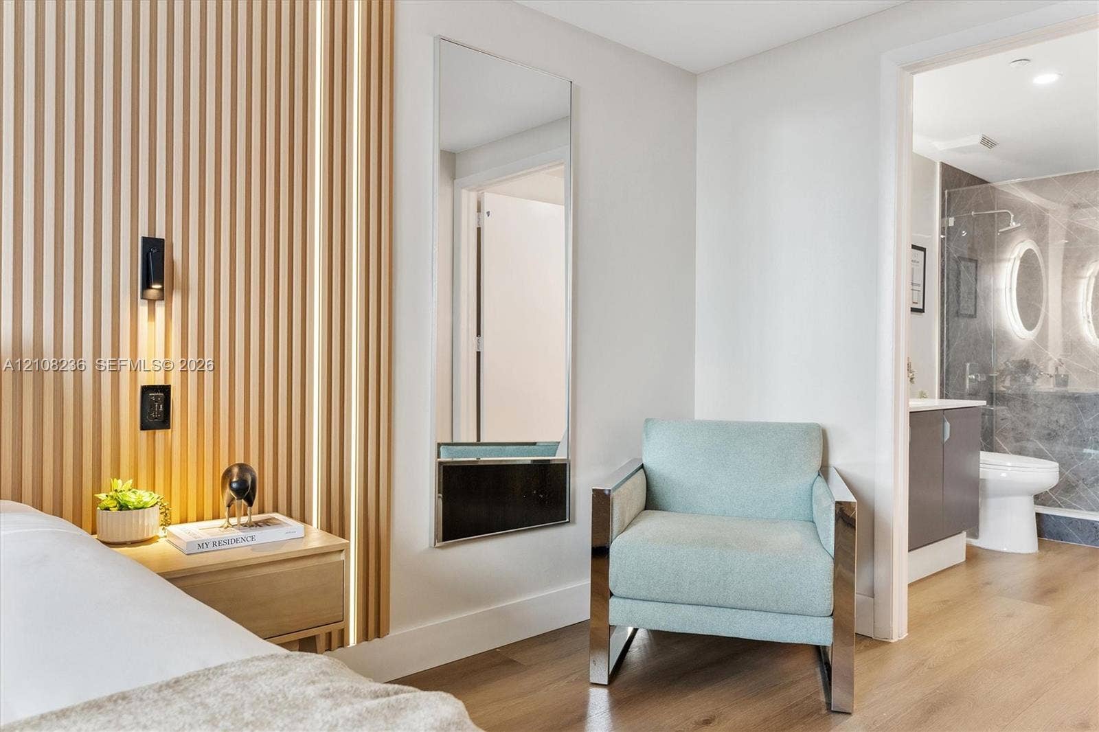 Vertical wood-slat accent wall with integrated linear lighting, wood-finish flooring, full-length wall mirror, and attached wall-mounted lighting fixture