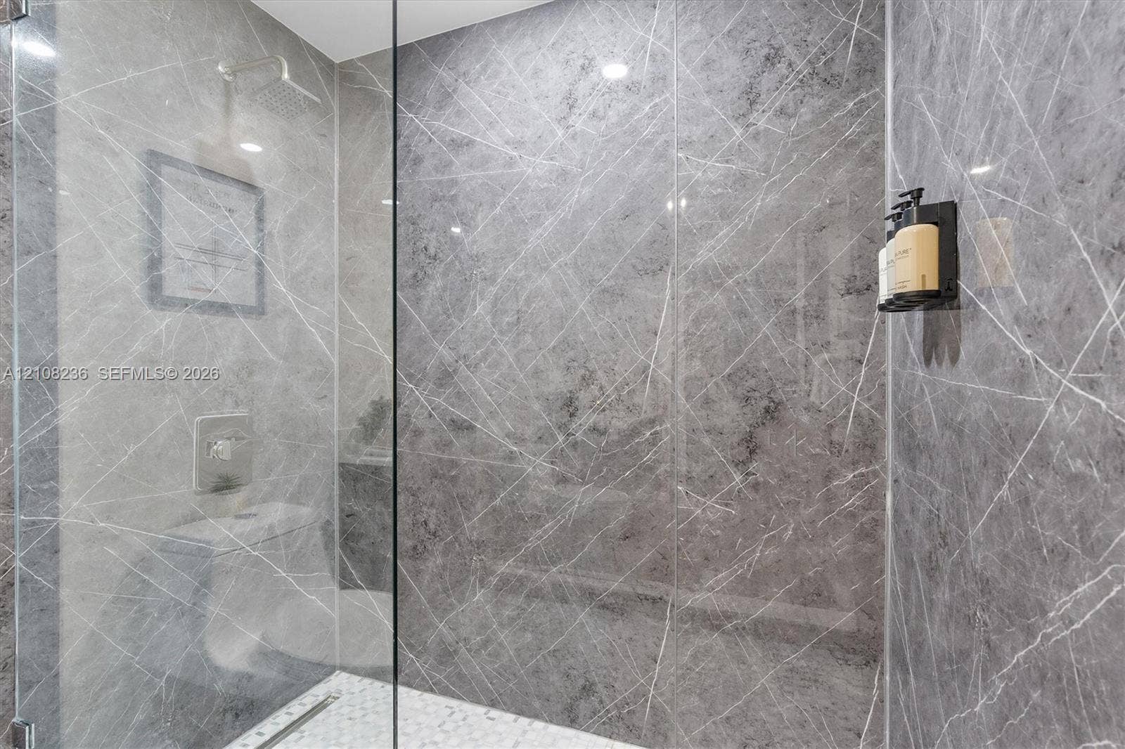 Walk-in shower featuring large-format grey veined tile wall surfacing, frameless glass enclosure, ceiling-mounted rainfall showerhead, and mosaic tile flooring