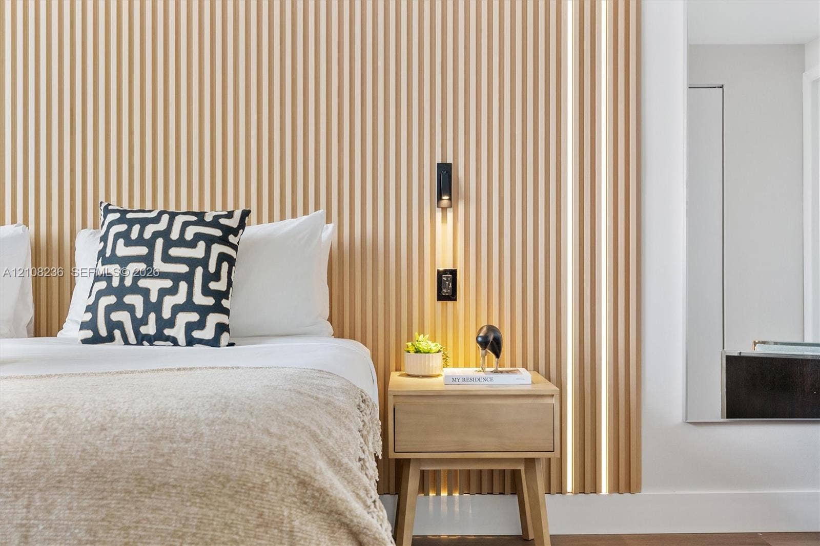 Floor-to-ceiling slatted wood wall paneling with integrated vertical LED accent lighting and a matte black wall-mounted reading light