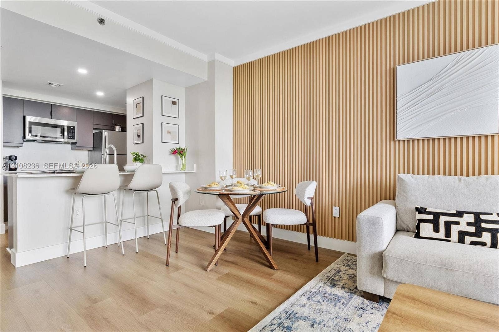 Vertical slat wood-finish accent wall, wood-finish flooring, and kitchen featuring dark cabinetry, stainless steel appliances, and a quartz countertop breakfast bar