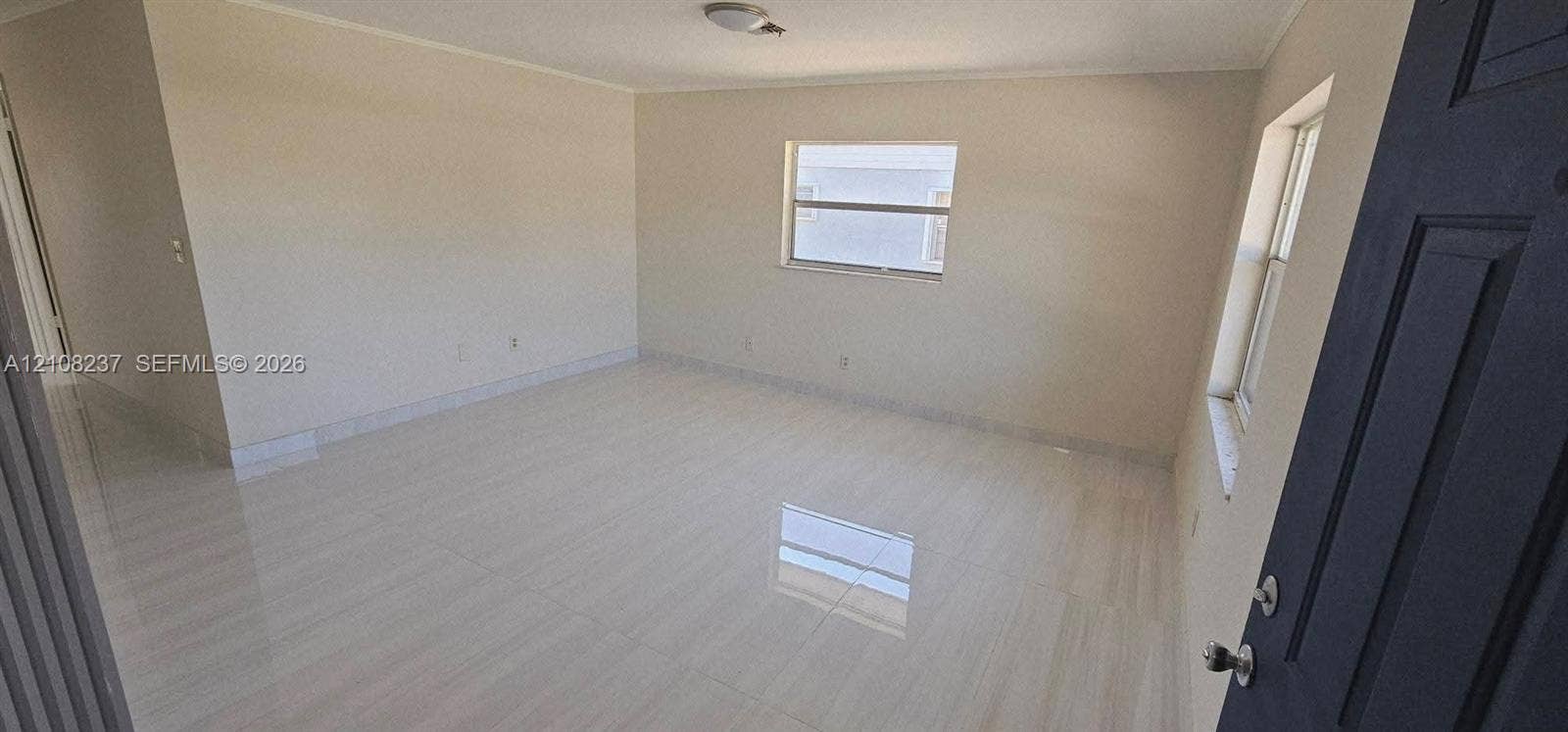 338 SW 8th Avenue SW, #., Vero Beach, Vero Beach, FL 32962 Interior space featuring light-toned tile flooring, neutral wall paint, two single-hung windows, and a multi-panel door with metallic hardware
