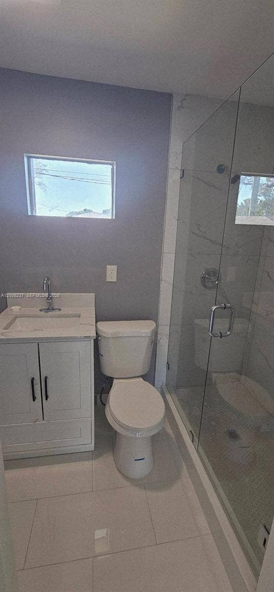 338 SW 8th Avenue SW, #., Vero Beach, Vero Beach, FL 32962 Bathroom featuring a white vanity cabinet with a stone-top integrated sink, polished chrome faucet, glass-enclosed shower with tiled walls, and large-format porcelain tile flooring