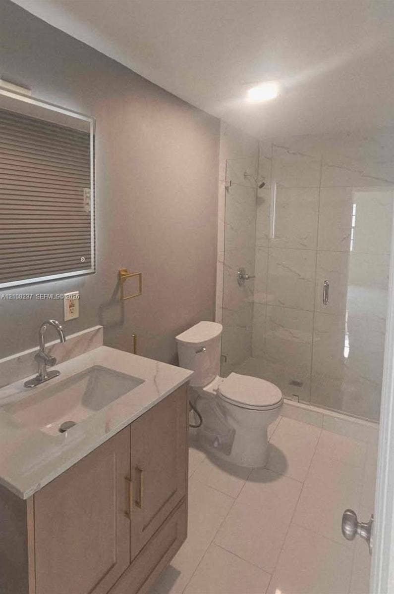 338 SW 8th Avenue SW, #., Vero Beach, Vero Beach, FL 32962 Bathroom featuring a wood-finish vanity with a stone-top integrated sink, wall-mounted mirror, walk-in shower with glass enclosure, and large-format tile flooring