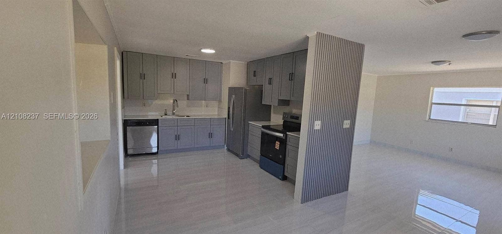 338 SW 8th Avenue SW, #., Vero Beach, Vero Beach, FL 32962 Kitchen featuring grey cabinetry, stainless steel appliances, neutral stone-finish tile flooring, and a decorative corrugated metal accent wall
