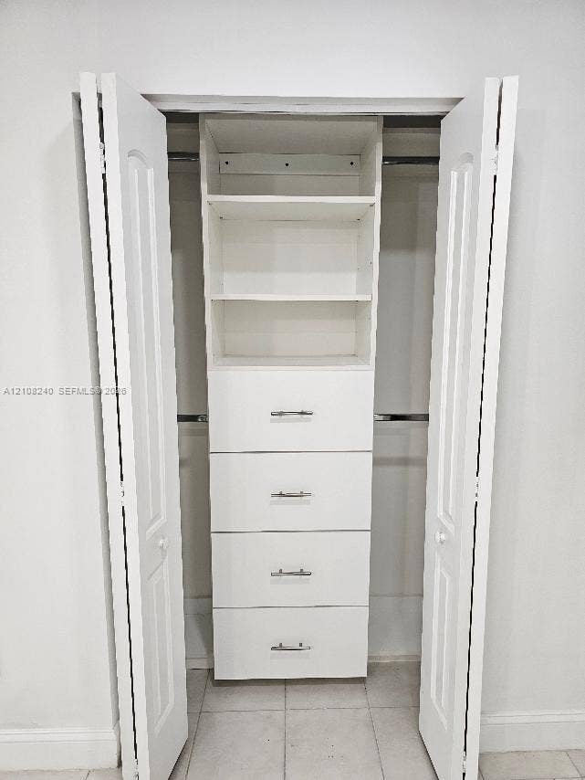Closet featuring white bi-fold doors, integrated shelving, four drawers with metallic hardware, and dual clothing rods