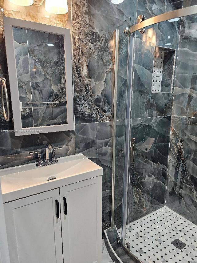 Bathroom featuring large-format dark patterned wall tiling, white vanity with rectangular basin, chrome faucet, shower enclosure with sliding glass door, and integrated shower wall niche