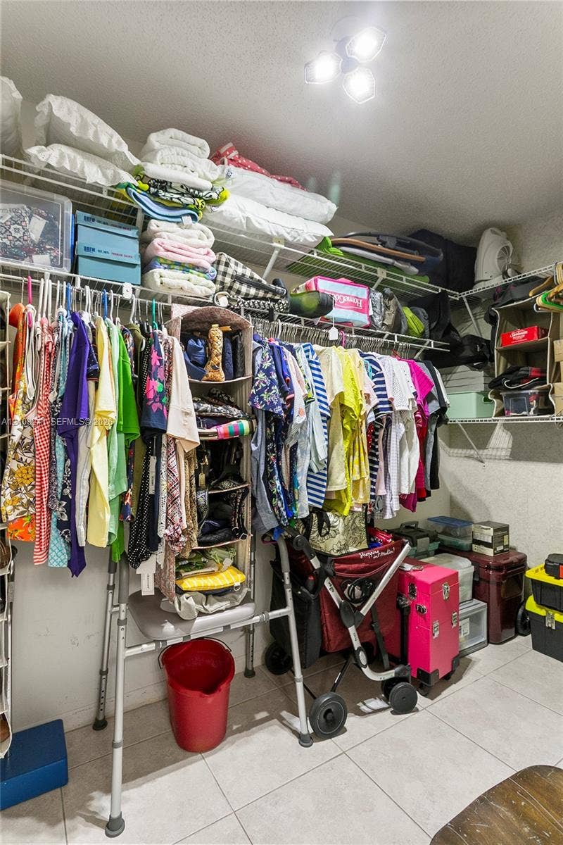 Walk-in closet featuring wire shelving, triple-tiered storage racks, tile flooring, and flush-mount overhead lighting