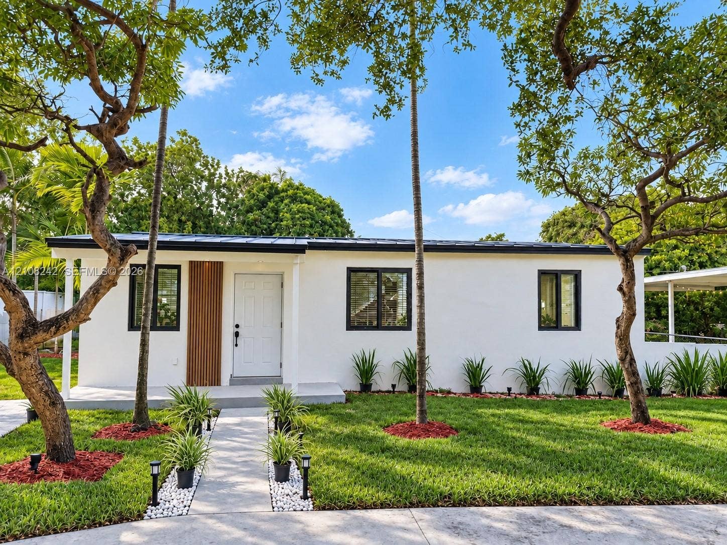61 E 39th Street, Hialeah, FL 33013 Stucco exterior featuring vertical wood-slat accent paneling, a dark metal roof, black-framed windows, and a paved walkway with stone borders