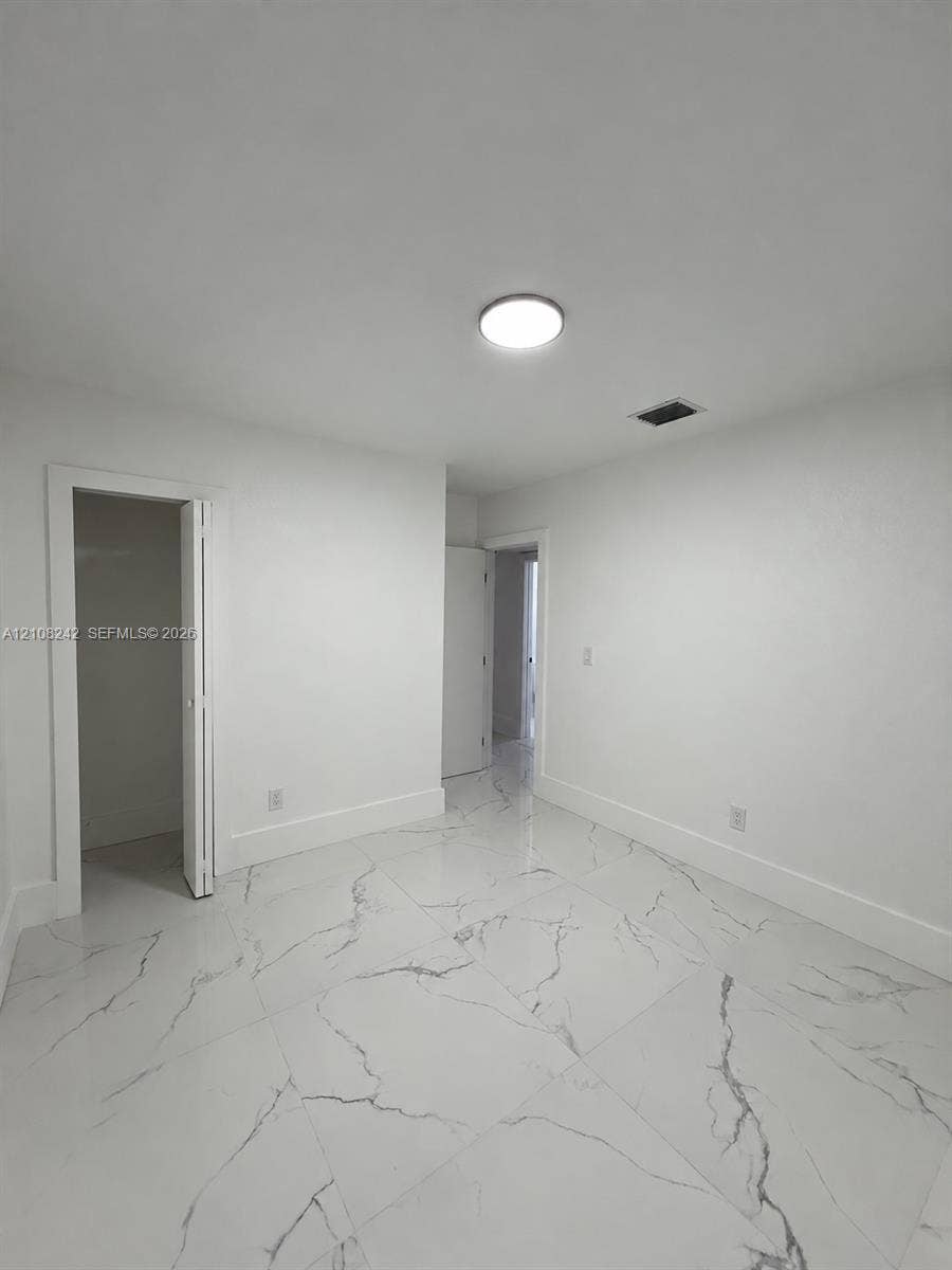 61 E 39th Street, Hialeah, FL 33013 Neutral-toned interior space featuring large-format white stone-finish tile flooring with grey veining, a flush-mount circular ceiling light, and a built-in closet with bi-fold doors