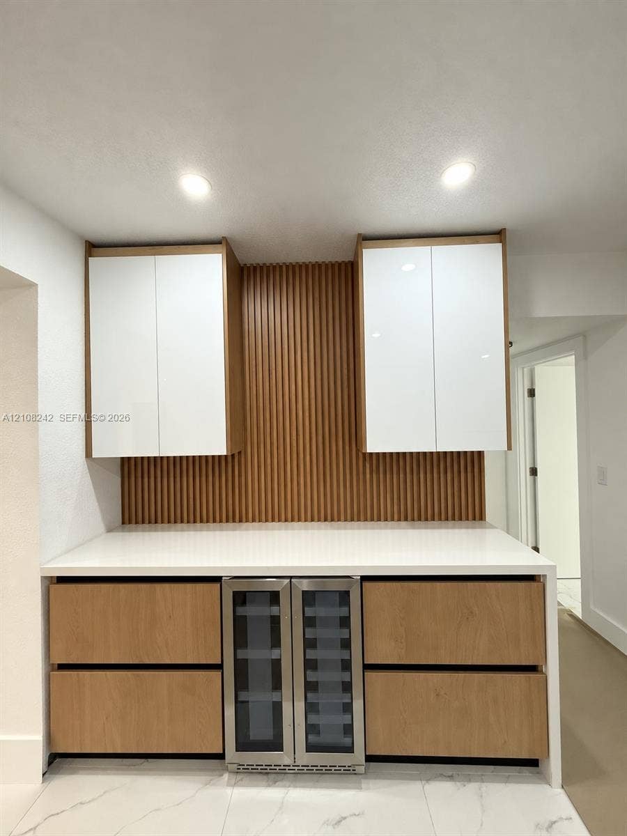61 E 39th Street, Hialeah, FL 33013 Custom built-in cabinetry featuring white gloss upper cabinets, wood-finish lower drawers, integrated wine refrigerator, white stone-surface countertop, and vertical wood slat backsplash