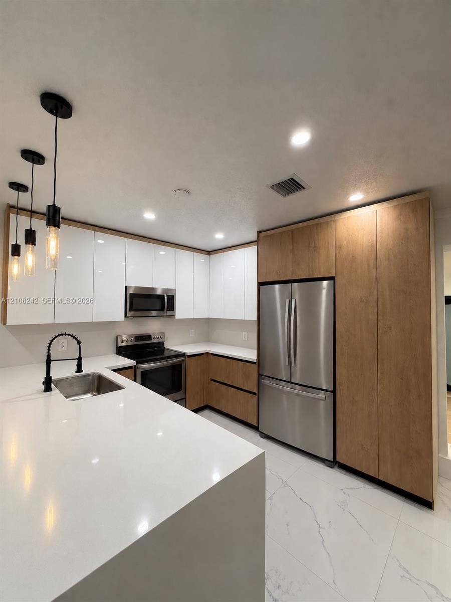 61 E 39th Street, Hialeah, FL 33013 Kitchen featuring white gloss cabinetry, wood-finish lower cabinets, quartz countertops, stainless steel appliances, and matte black pendant lighting