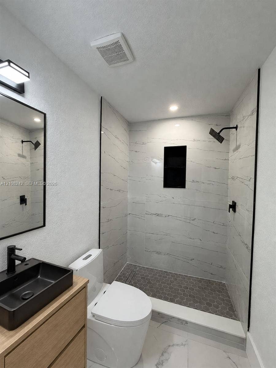61 E 39th Street, Hialeah, FL 33013 Walk-in shower featuring large-format tile surround, integrated recessed shelving, and a hexagonal tile floor