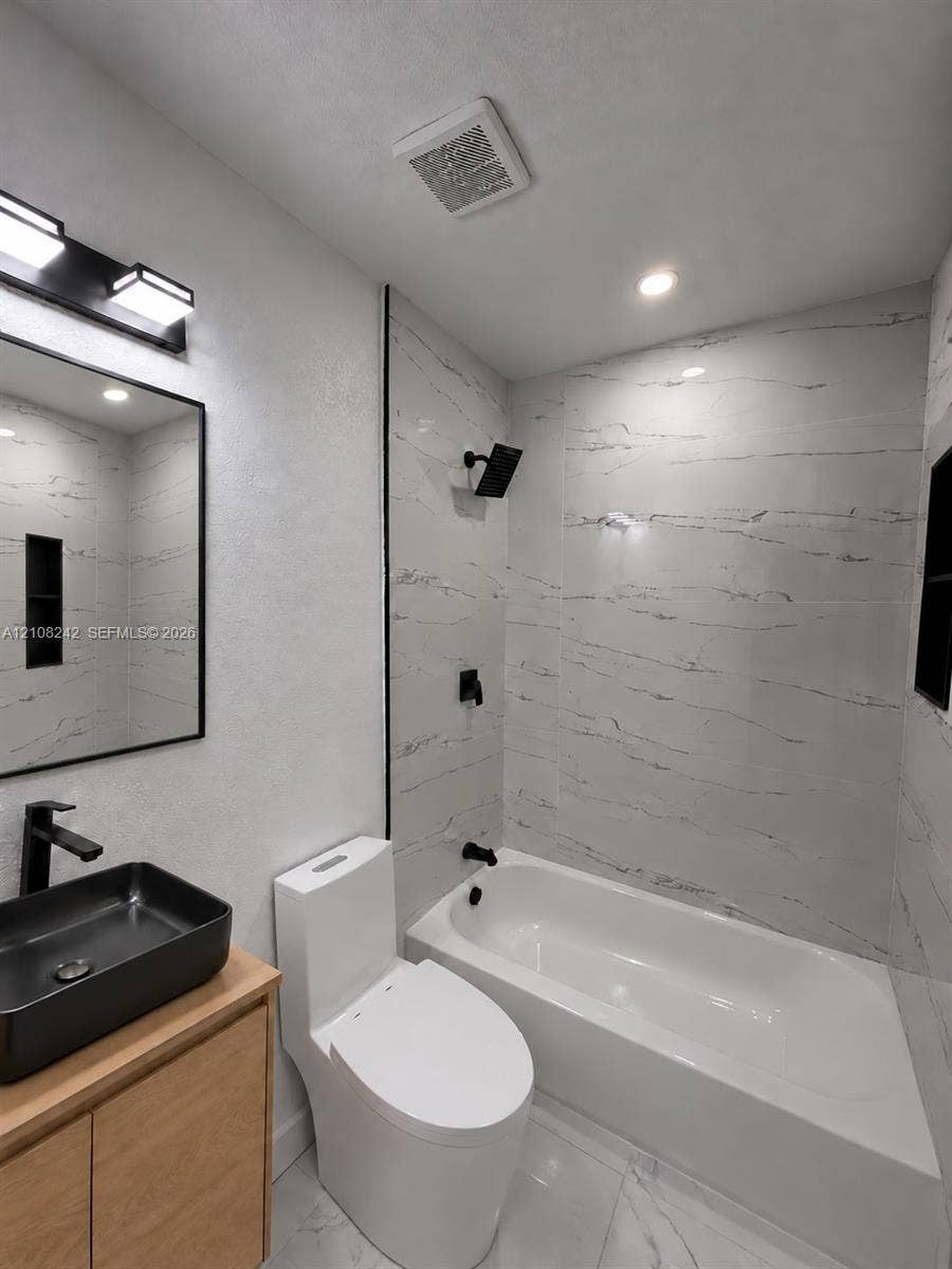 61 E 39th Street, Hialeah, FL 33013 Bathroom featuring a wood-finish vanity, matte black fixtures, rectangular vessel sink, and full-height wall tile surrounding the bathtub