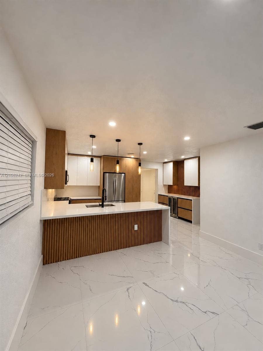 61 E 39th Street, Hialeah, FL 33013 Kitchen featuring custom two-tone cabinetry with slatted wood detailing, white stone countertops, large-format veined porcelain tile flooring, stainless steel built-in appliances, and pendant lighting