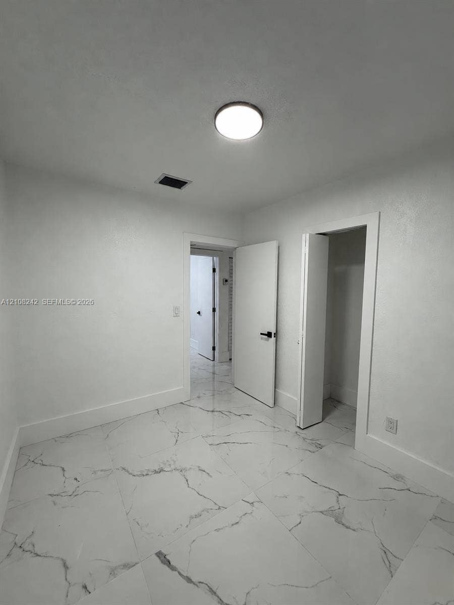 61 E 39th Street, Hialeah, FL 33013 Large-format stone-style tile flooring with veining, solid-core interior doors, matte black hardware, and a flush-mount LED ceiling fixture
