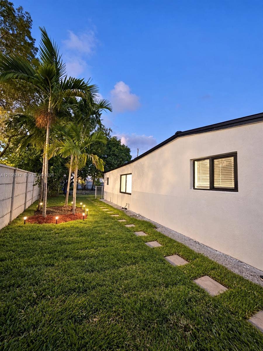 61 E 39th Street, Hialeah, FL 33013 Side yard featuring a manicured lawn, established palm trees, a concrete block privacy wall, stone paver pathway, and recessed landscape lighting