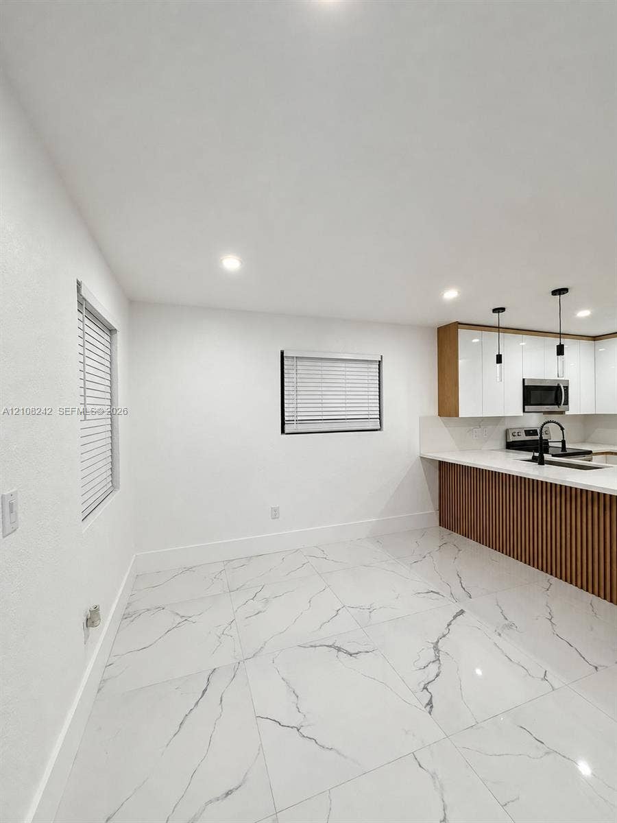 61 E 39th Street, Hialeah, FL 33013 Large-format tile flooring, white gloss cabinetry, vertical wood-slat kitchen island detailing, matte black fixtures, and recessed ceiling lighting