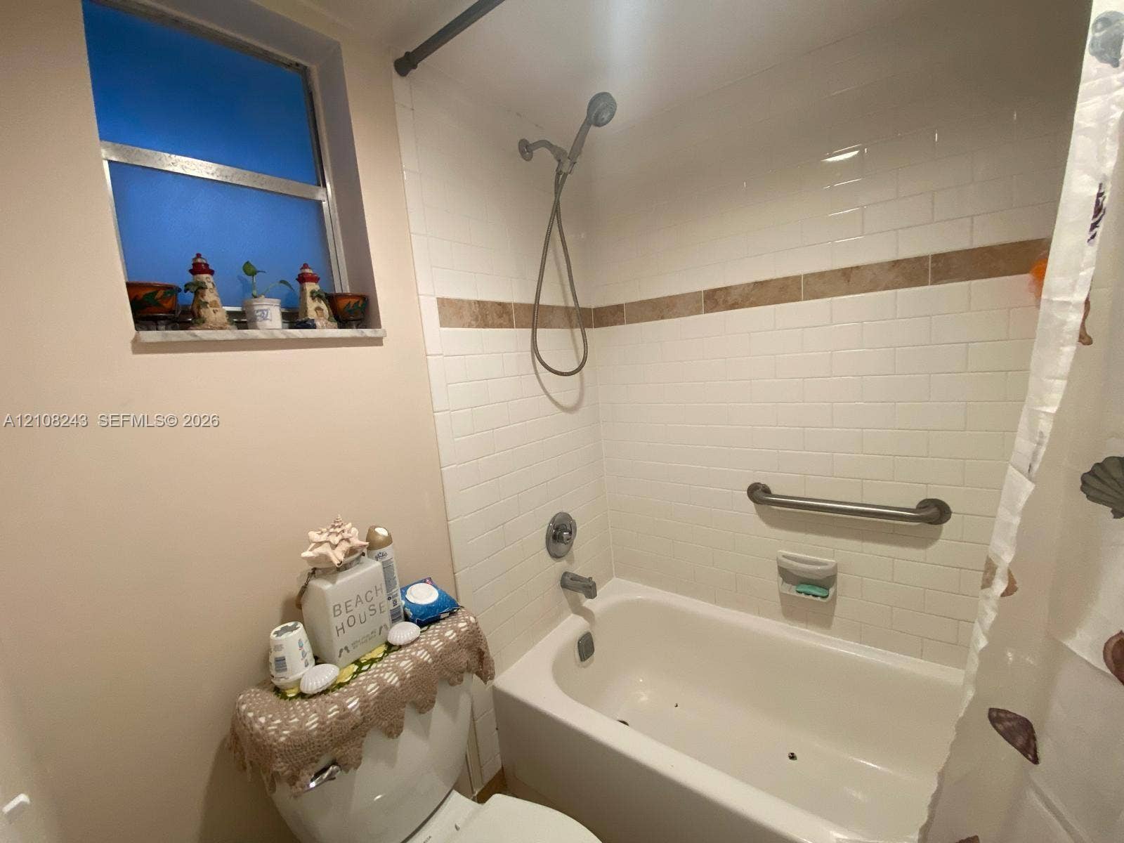 6505 Winfield Boulevard, #B-16, Margate, FL 33063 Bathtub with white subway tile surround, decorative tile inlay, adjustable shower head, and wall-mounted grab bar, complemented by a stone-finish window sill