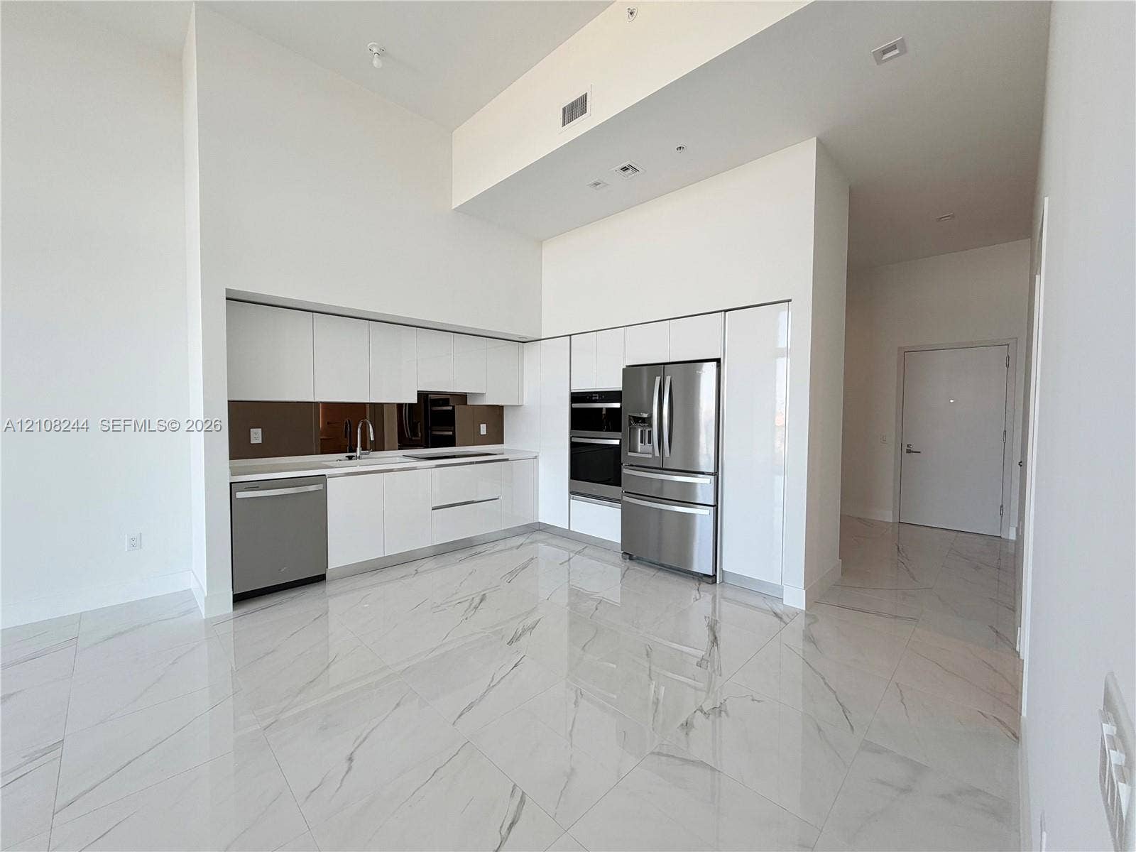 1170 Hallandale Beach Boulevard, #605, Hallandale Beach, Hallandale Beach, FL 33009 Kitchen featuring high-gloss white cabinetry, stainless steel appliances, built-in wall oven, metallic backsplash, and large-format porcelain tile flooring