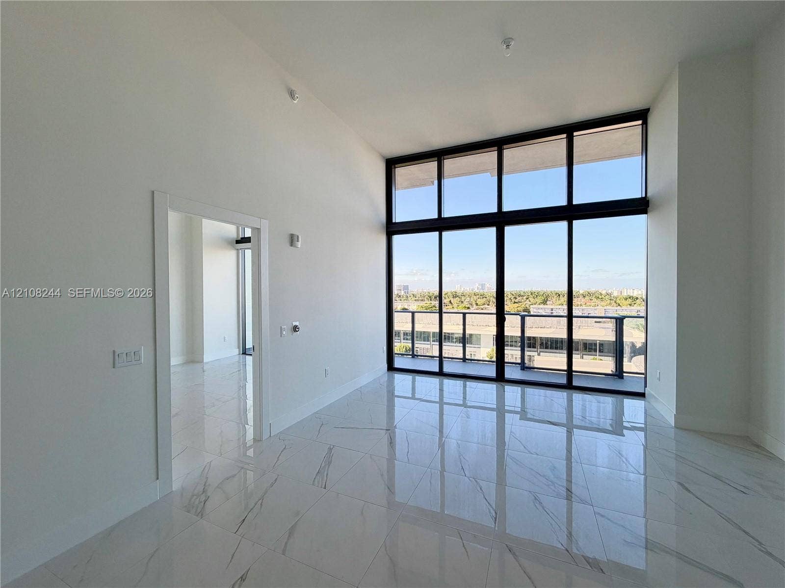 1170 Hallandale Beach Boulevard, #605, Hallandale Beach, Hallandale Beach, FL 33009 High-ceiling living area featuring large-format polished stone-finish flooring, floor-to-ceiling windows with dark framing, and a private balcony
