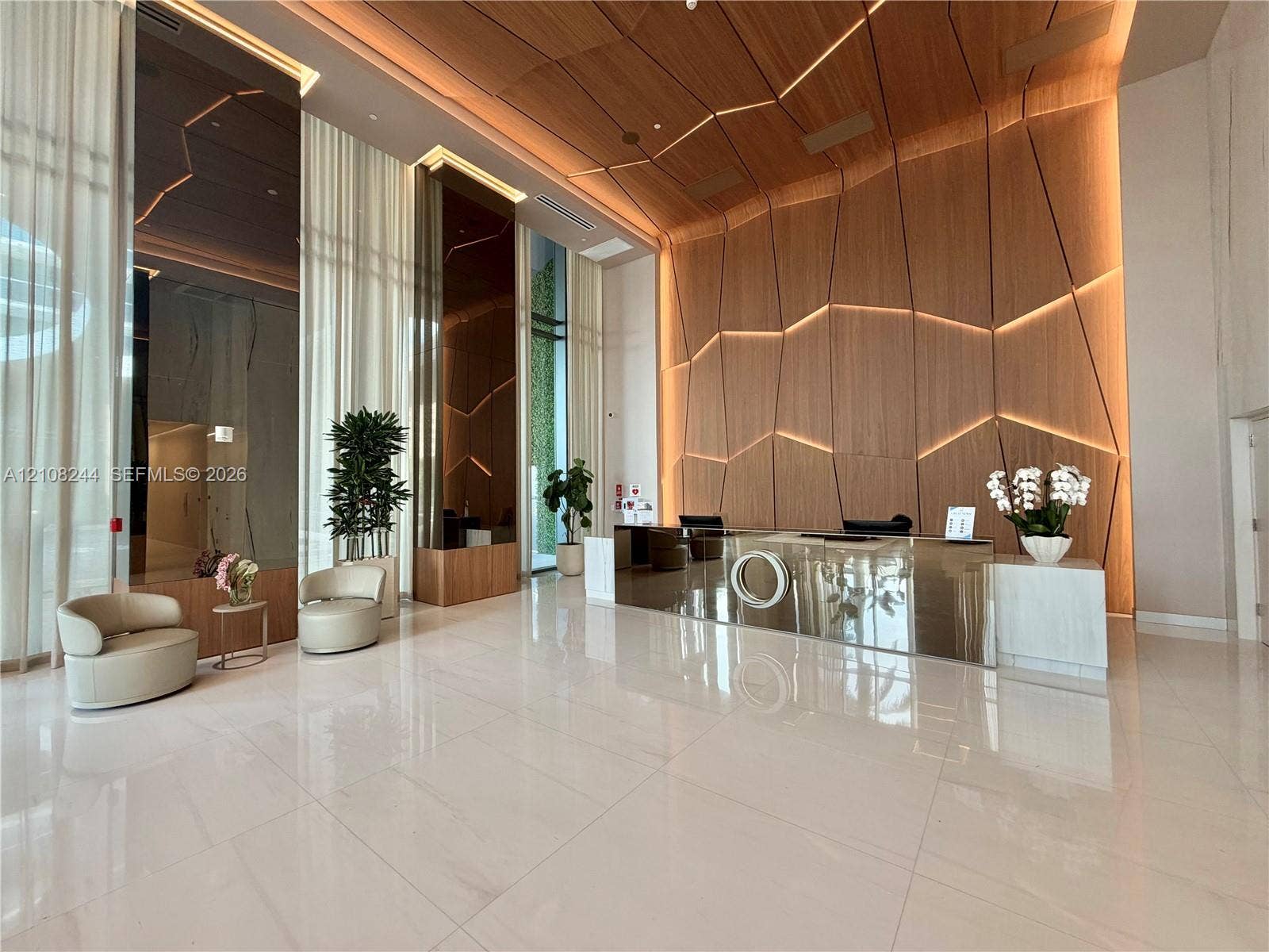 1170 Hallandale Beach Boulevard, #605, Hallandale Beach, Hallandale Beach, FL 33009 Double-height ceiling, large-scale veined stone wall cladding, floor-to-ceiling windows, custom tiered pendant lighting, and a floor-to-ceiling illuminated water feature with a central vertical moss panel