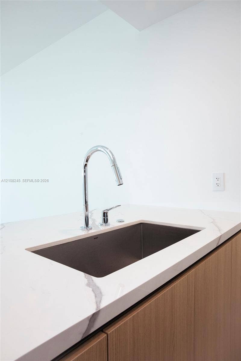 Undermount stainless steel kitchen sink with a high-arch chrome pull-down faucet, stone-finish countertop with veining, and flat-panel wood-finish cabinetry