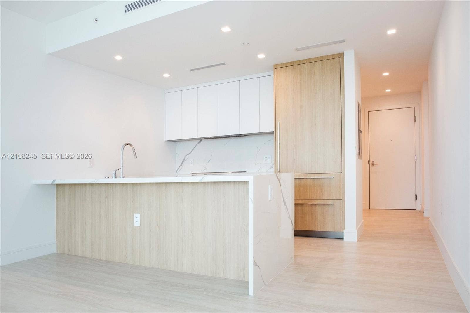 Kitchen featuring wood-finish cabinetry, white matte upper cabinets, stone-surfaced island with waterfall edge, integrated refrigerator, and recessed lighting