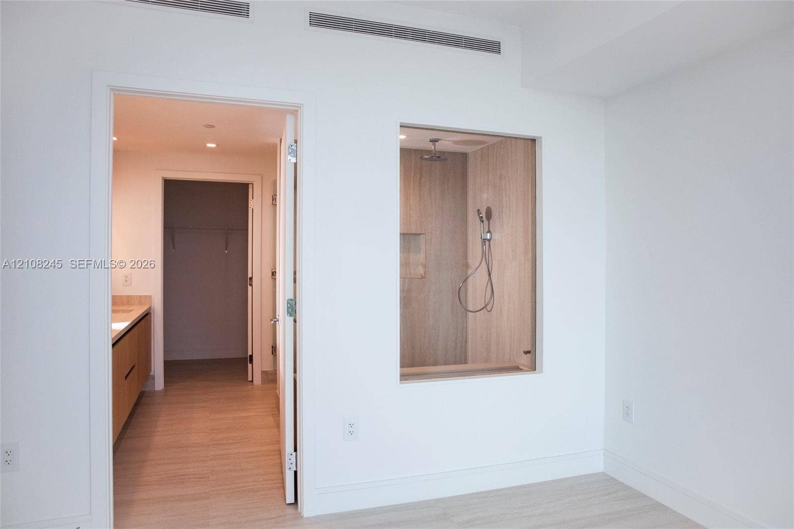 Shower enclosure with a glass partition, wall-mounted shower head, and built-in wall niche, featuring wood-finish wall tile and wood-finish flooring