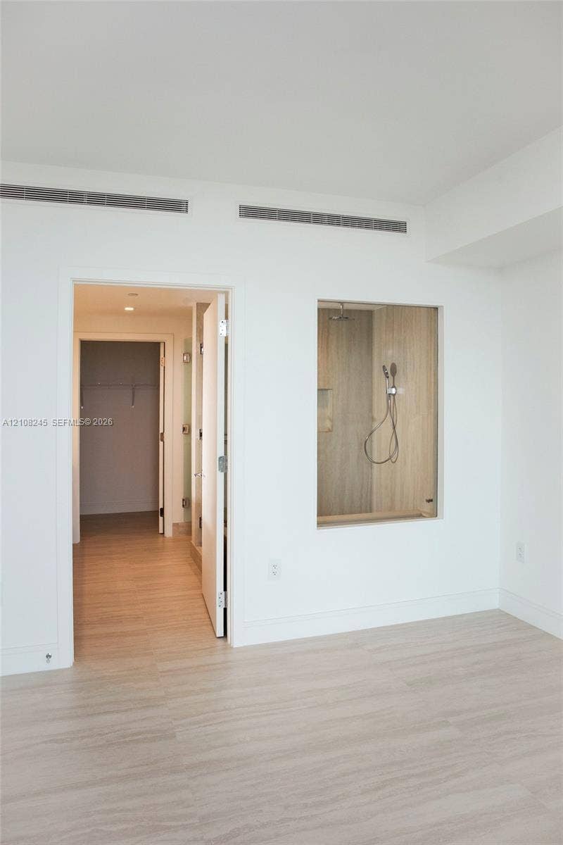 Wood-finish flooring, glass-enclosed shower stall with neutral tile surround, and recessed ceiling lighting