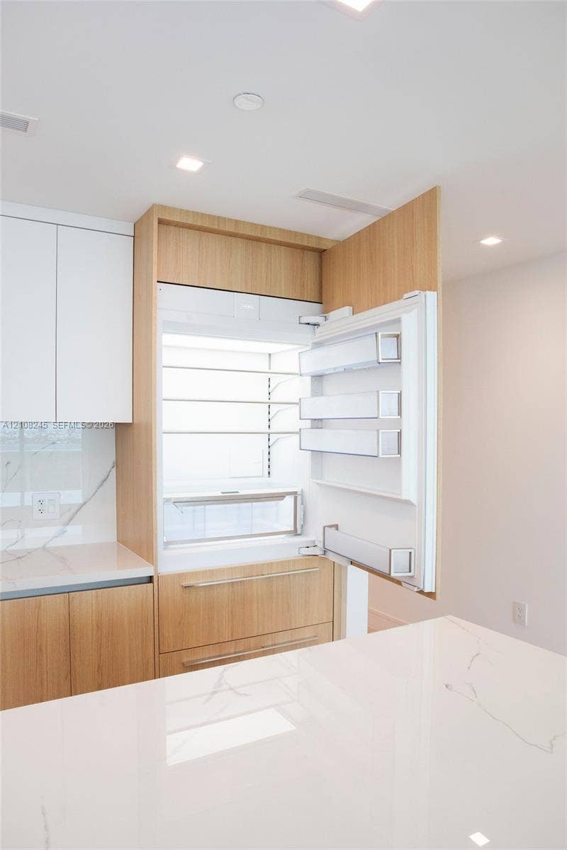 Integrated panel-ready refrigerator, custom wood-finish cabinetry, solid-surface countertop with veining, and recessed lighting
