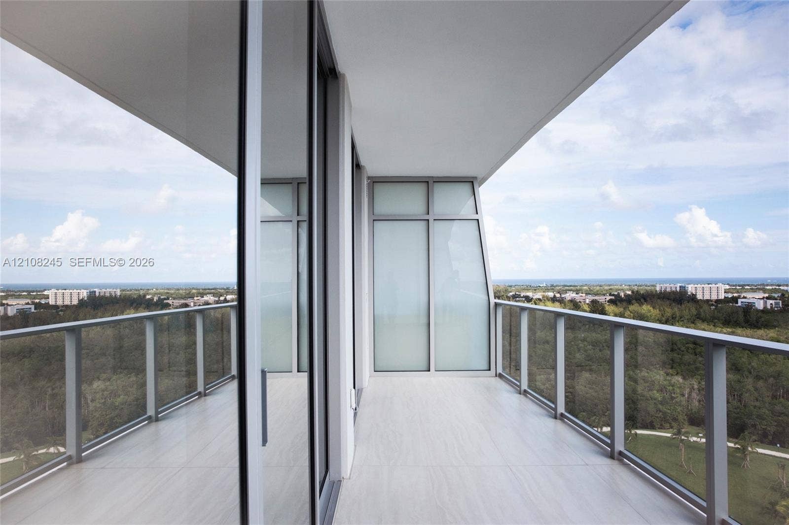 Covered balcony featuring expansive glass panel railings, floor-to-ceiling sliding glass doors, and tiled flooring