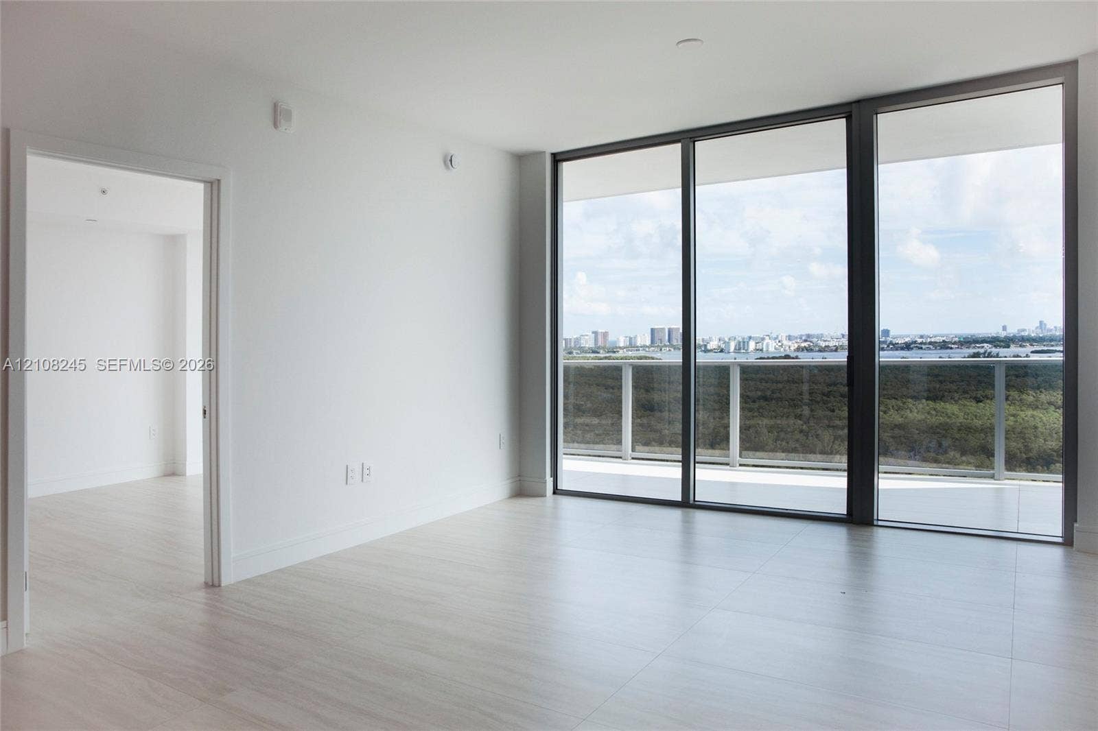 Floor-to-ceiling glass panel windows, light-toned tile flooring, and an integrated outdoor balcony with a metal railing