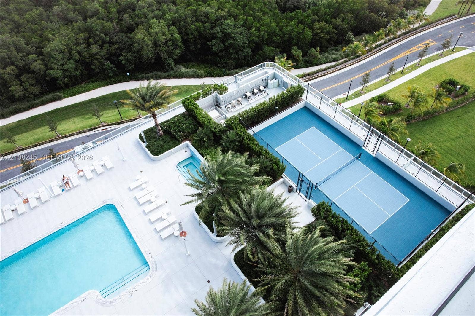 Outdoor recreation area featuring a tennis court, swimming pool, spa, and mature palm tree landscaping