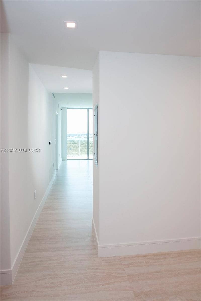 Hallway featuring light-toned flooring, recessed ceiling lighting, and floor-to-ceiling glass paneling
