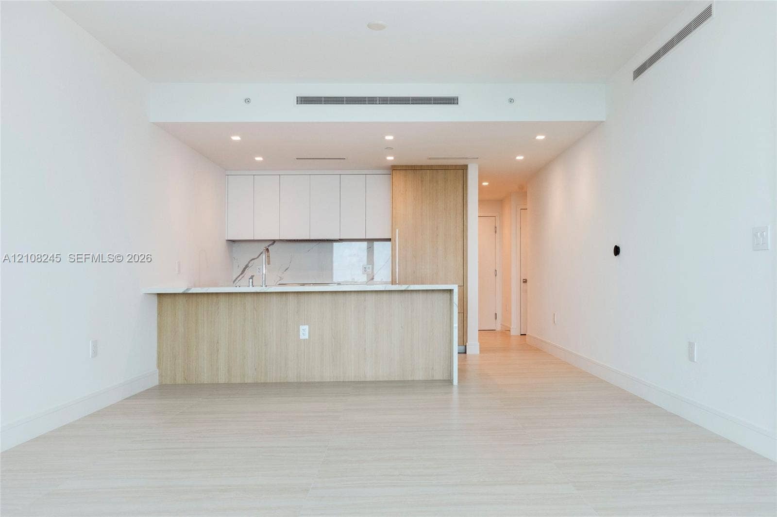 Kitchen featuring flat-panel cabinetry, light-toned wood-finish panels, stone-surface countertops, recessed ceiling lighting, and wood-finish flooring