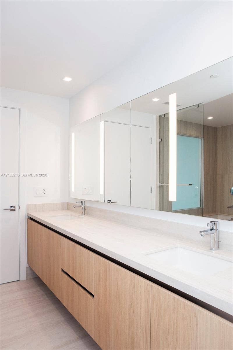 Floating wood-finish double vanity featuring integrated rectangular sinks, expansive countertop, full-width mirror with integrated lighting, and polished chrome faucets