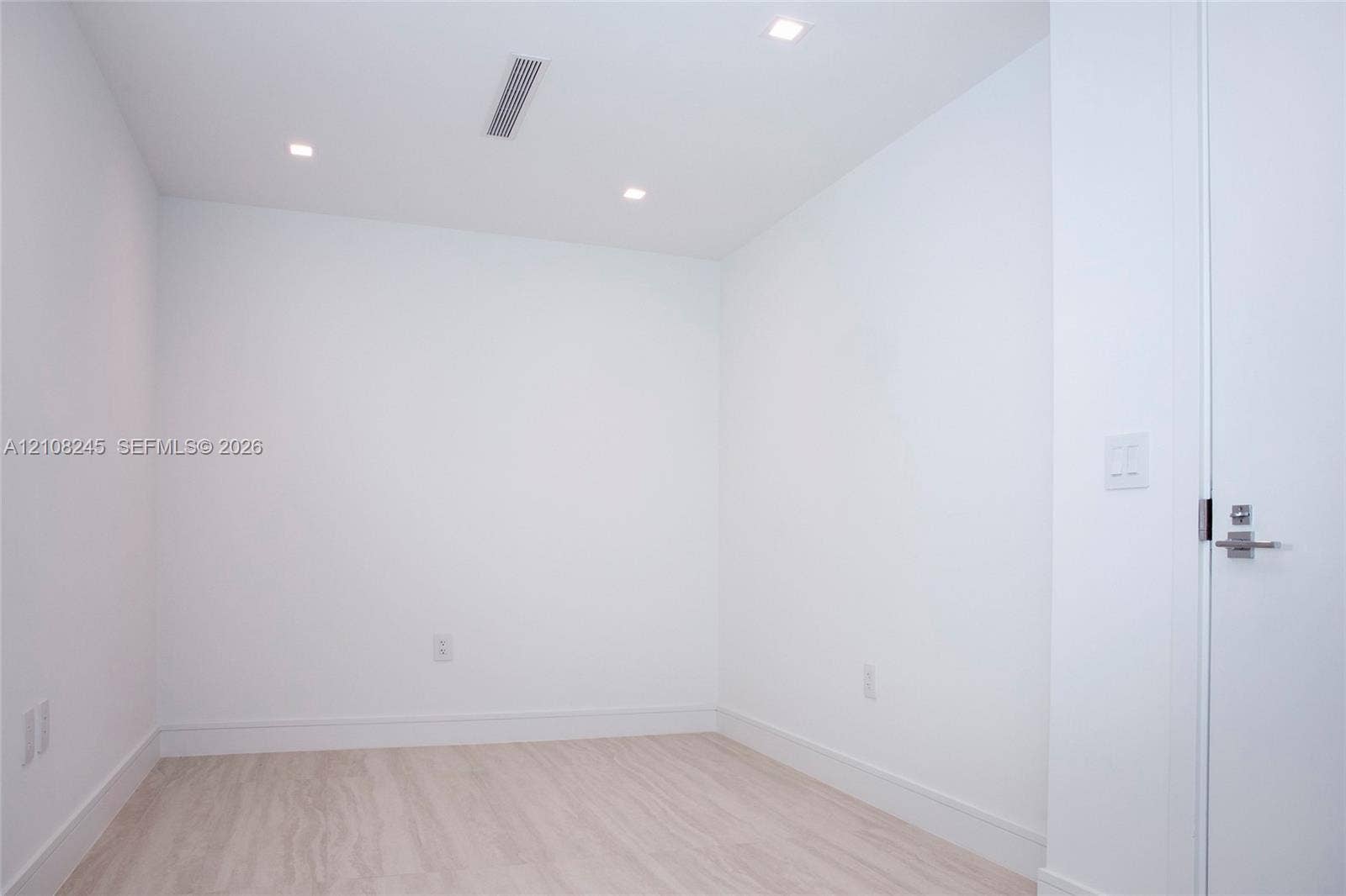 Minimalist interior featuring white wall finishes, wood-finish flooring, and recessed ceiling lighting