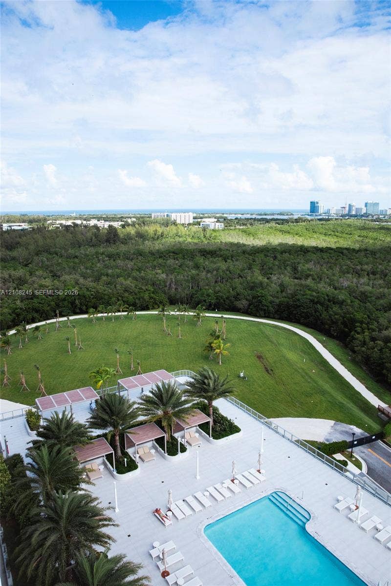 Pool deck featuring a swimming pool, multiple shaded cabanas, mature palm trees, and expansive grassy grounds