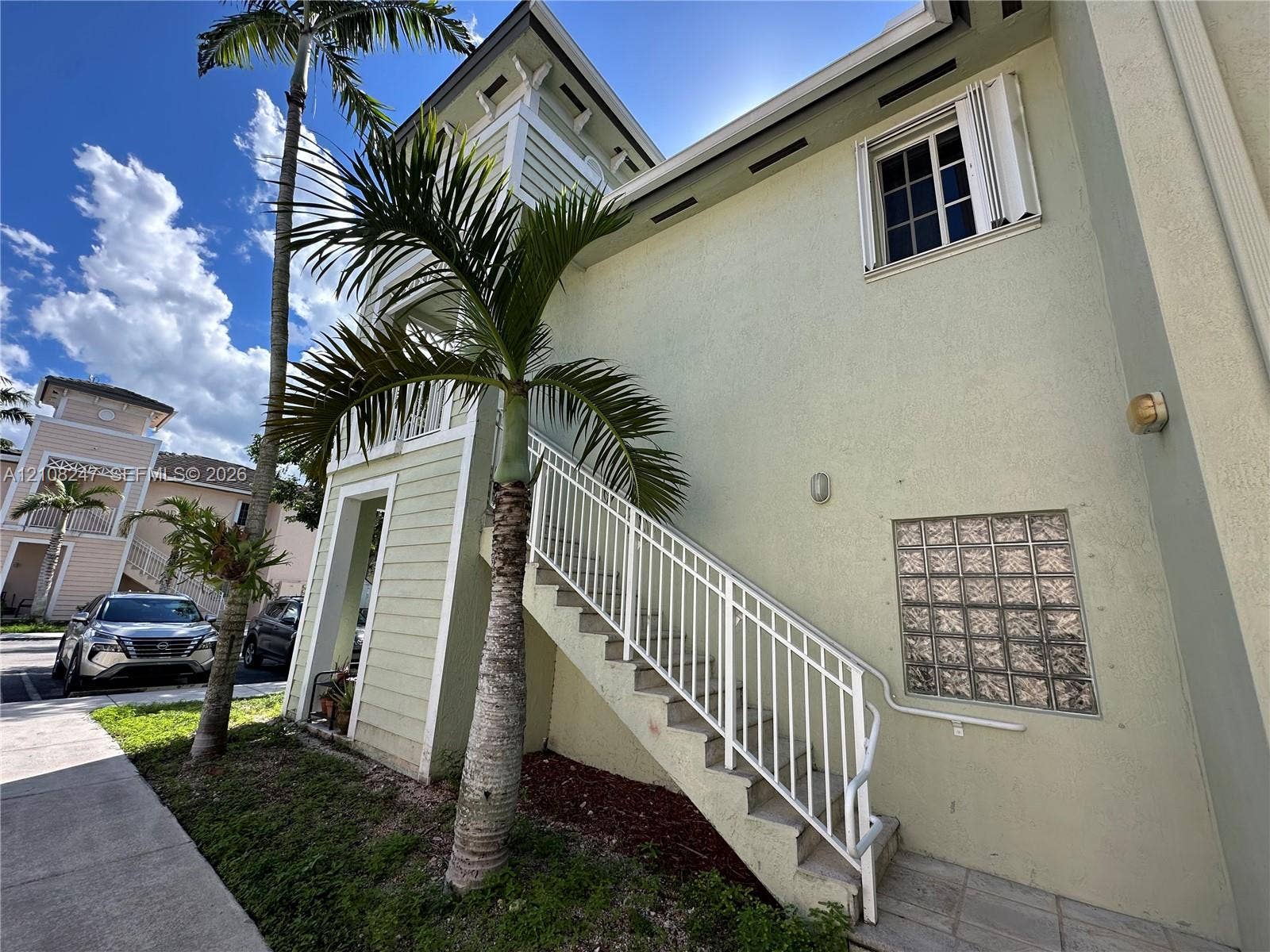 2641 NE 4th Street, #204, Homestead, Homestead, FL 33033 Multi-story exterior featuring light-toned stucco siding, metal-railing stairwell, glass block accent window, and exterior wall-mounted lighting