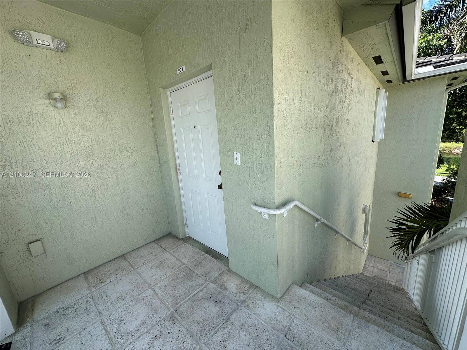 2641 NE 4th Street, #204, Homestead, Homestead, FL 33033 Covered entryway featuring textured stucco exterior walls, tiled flooring, wall-mounted lighting, and a white six-panel entry door