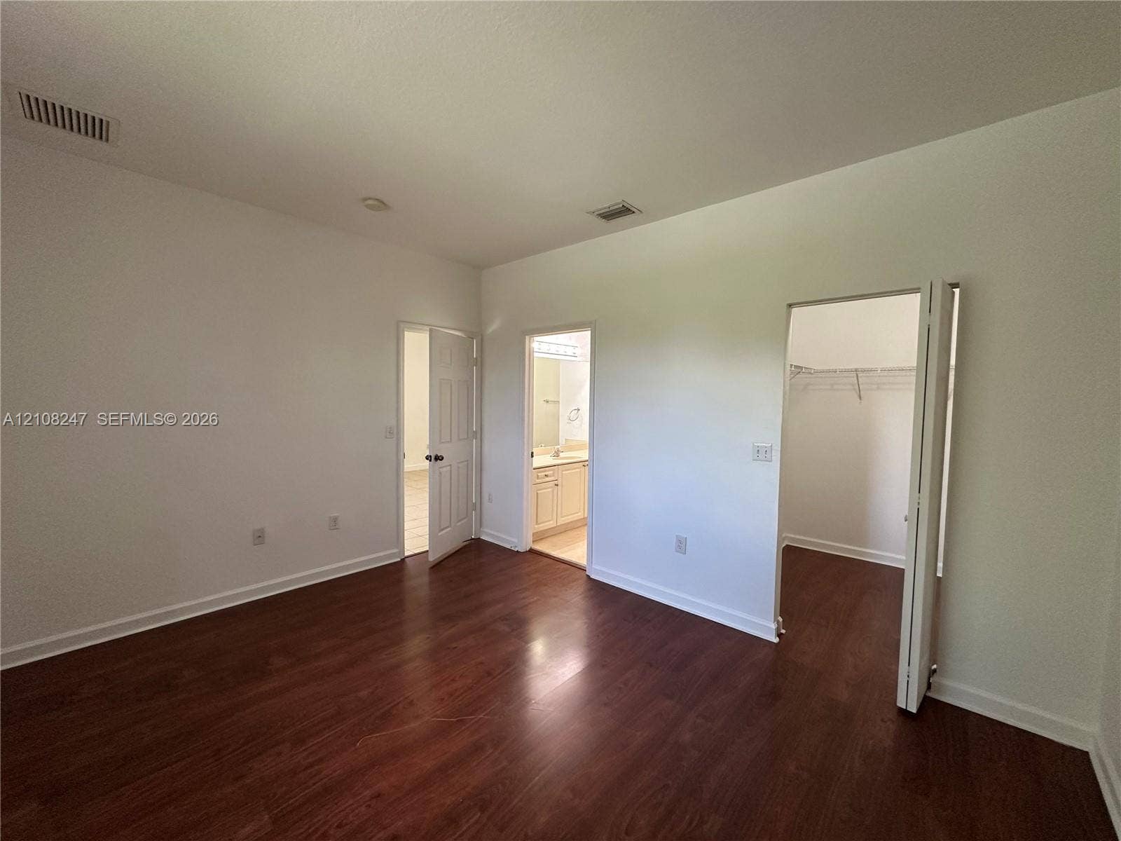 2641 NE 4th Street, #204, Homestead, Homestead, FL 33033 Room featuring wood-finish flooring, two six-panel interior doors, and a walk-in closet with built-in wire shelving