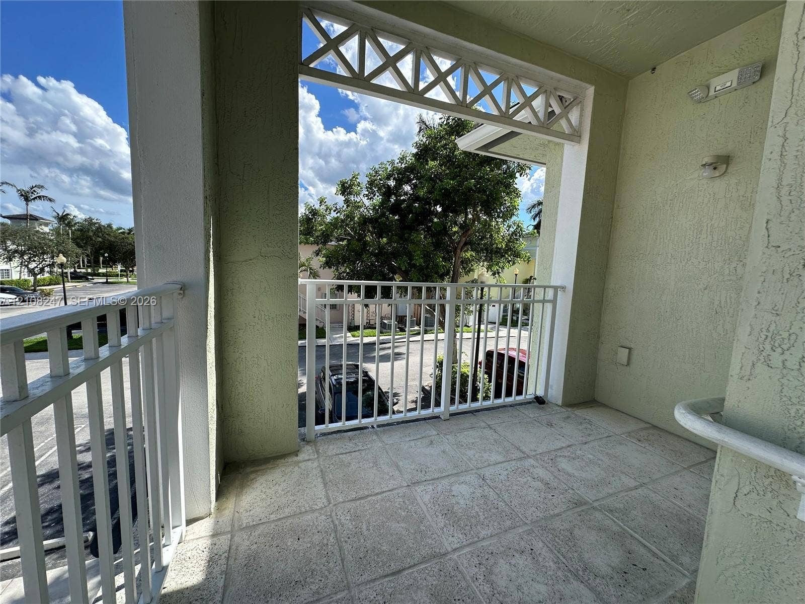 2641 NE 4th Street, #204, Homestead, Homestead, FL 33033 Covered balcony featuring tiled flooring, white metal railings, decorative lattice woodwork, and stucco wall finishes