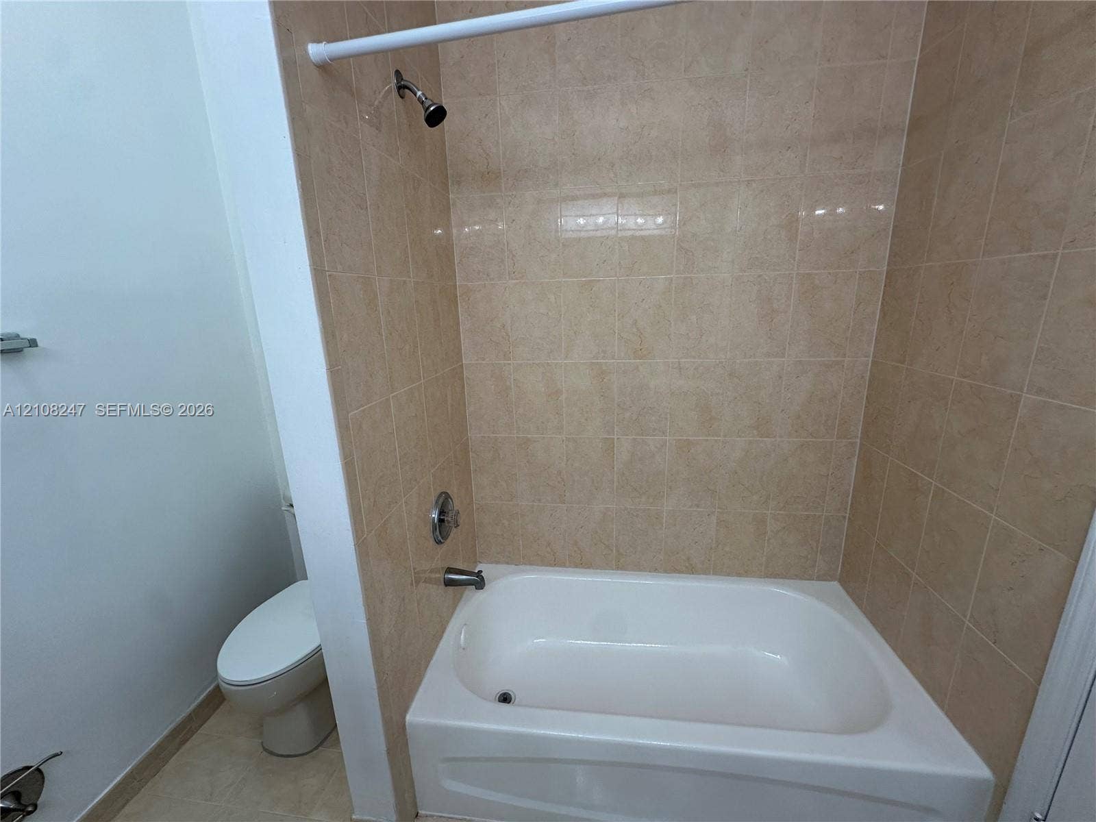 2641 NE 4th Street, #204, Homestead, Homestead, FL 33033 Bathtub with a white acrylic surround, tan wall-tile finish, showerhead, and a standard-height toilet