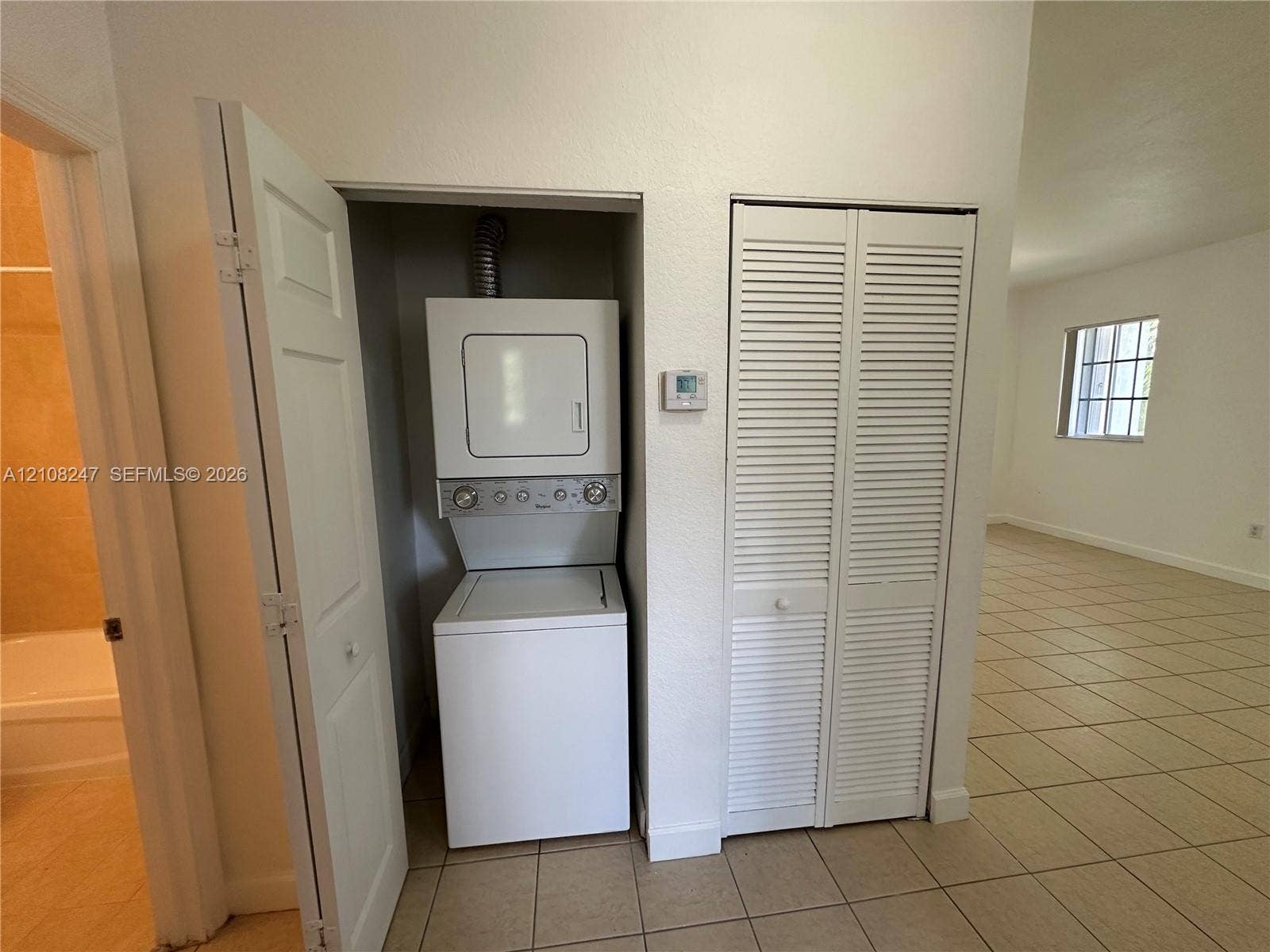 2641 NE 4th Street, #204, Homestead, Homestead, FL 33033 Laundry closet featuring a stackable washer and dryer unit, louvered bi-fold doors, and tile flooring