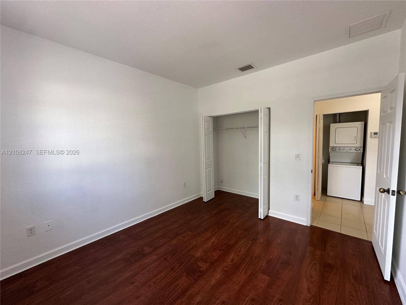 2641 NE 4th Street, #204, Homestead, Homestead, FL 33033 Room with wood-finish flooring, bi-fold closet doors, and attached utility area featuring a stacked laundry unit
