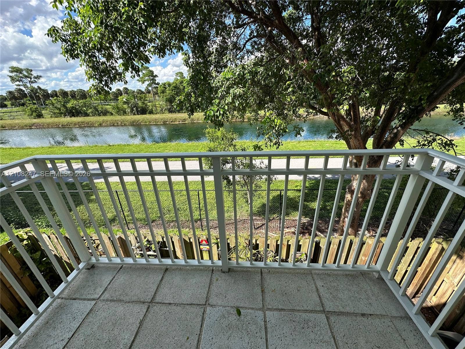 2641 NE 4th Street, #204, Homestead, Homestead, FL 33033 Balcony featuring white aluminum railings, light-toned concrete tile flooring, and a backdrop of mature trees overlooking a canal