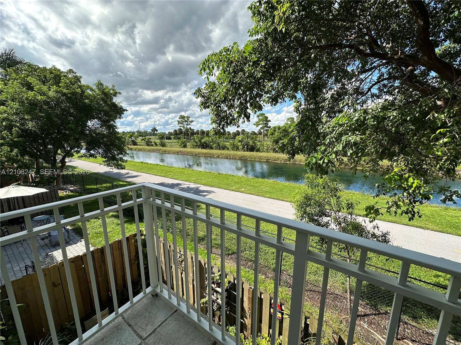 2641 NE 4th Street, #204, Homestead, Homestead, FL 33033 Elevated balcony with a white metal railing, paved patio area, wood fencing, and water frontage