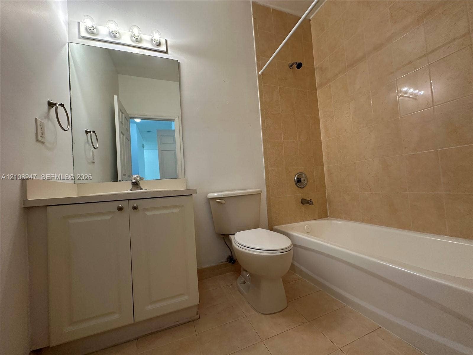 2641 NE 4th Street, #204, Homestead, Homestead, FL 33033 Bathroom featuring a vanity cabinet with a countertop basin, a wall-mounted mirror with a four-light fixture, and a tub with tiled surround