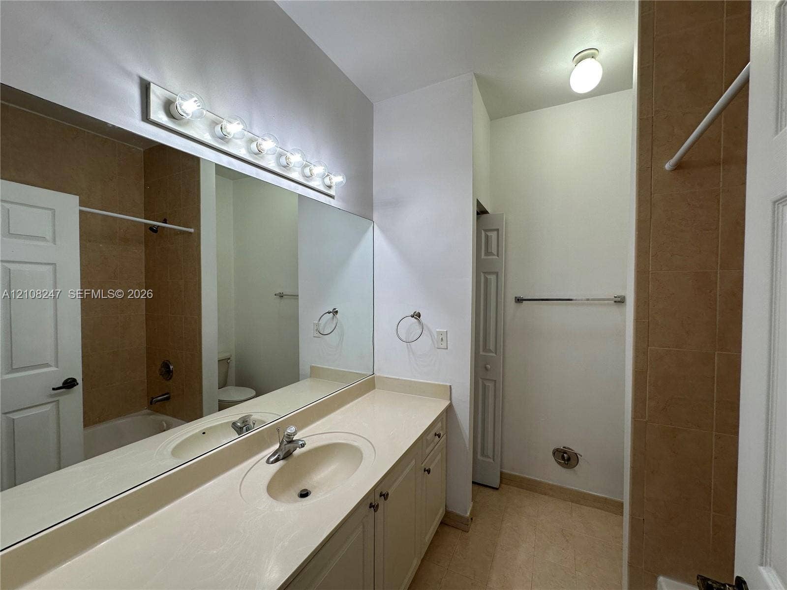 2641 NE 4th Street, #204, Homestead, Homestead, FL 33033 Bathroom featuring a neutral vanity with an integrated sink, a full-width vanity mirror, a six-bulb wall-mounted light fixture, and tile-surround tub area